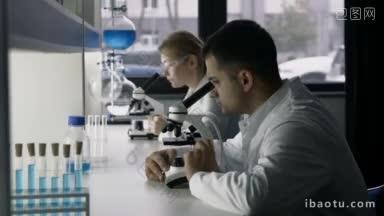 两个年轻的研究科学家在现代实验室通过显微镜研究新物质或病毒英俊年轻的混合种族科学家
